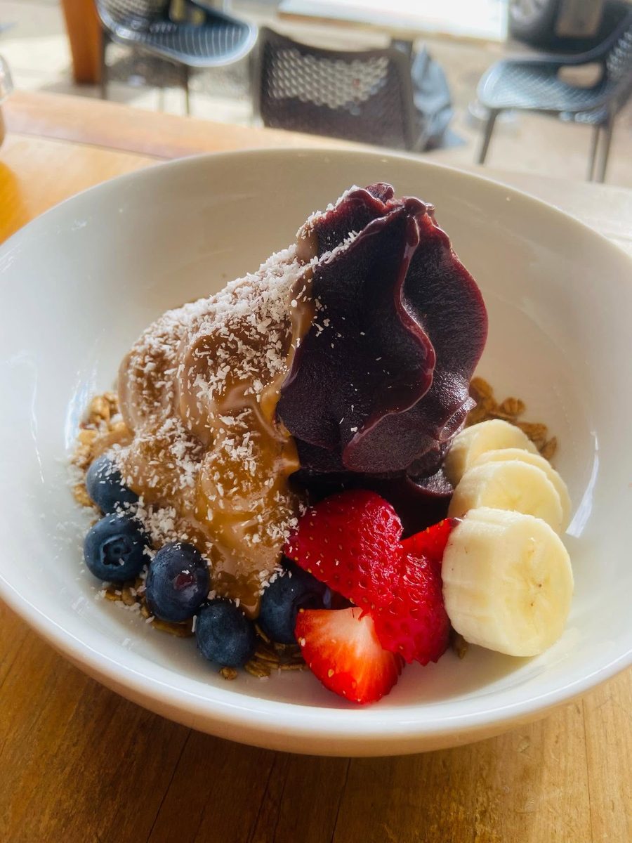 An acai bowl: a swirl of dark purple acai and nut butter over granola, topped with banana, strawberry, blueberries and shredded coconut.